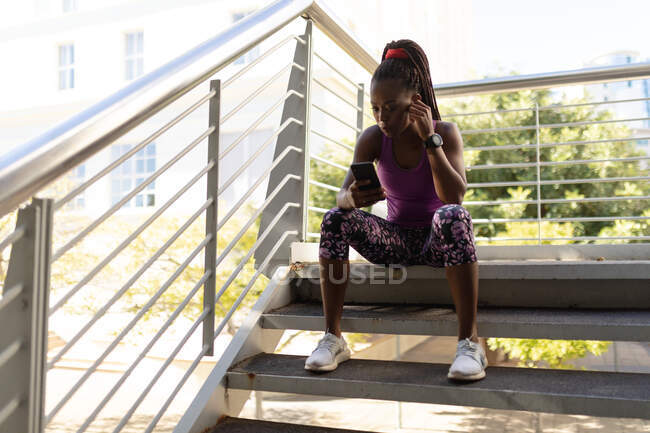Fit Afrikanische Amerikanerin sitzt auf Stufen und checkt Smartphone während des Trainings in der Stadt. gesunder urbaner aktiver Lebensstil und Outdoor-Fitness. — Stockfoto