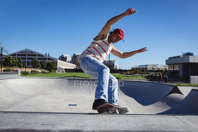 Hombre caucásico saltando y patinando en un día soleado. pasando el rato en skatepark urbano en verano. - foto de stock