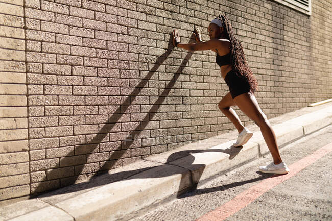 Жирна афро-американська жінка, що тягнеться схилившись до цегляної стіни, займається спортом у місті. Здоровий міський активний спосіб життя і зовнішній вигляд. — стокове фото