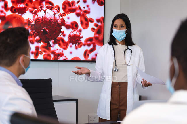 Жінка-лікар, яка носить маску для обличчя, дає презентацію команді лікарів у кімнаті для переговорів. охорона здоров'я та медичні дослідження під час прихованої пандемії 19 — стокове фото