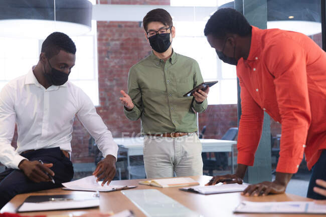 Team unterschiedlicher männlicher und weiblicher Bürokollegen mit Gesichtsmasken diskutieren gemeinsam im Büro. Hygiene und soziale Distanzierung am Arbeitsplatz während der covid 19 Pandemie. — Stockfoto