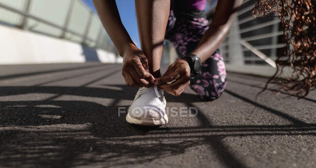 Нижняя часть женщины делает шнурки для обуви на пешеходном мосту, тренируясь в городе. здоровый активный образ жизни и фитнес. — стоковое фото