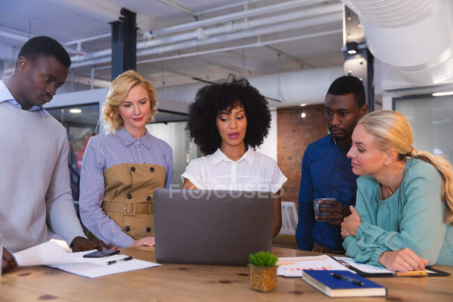 Equipe de diversos colegas de escritório discutindo juntos sobre um laptop no escritório moderno. conceito de negócio, profissionalismo, escritório e trabalho em equipe — Fotografia de Stock