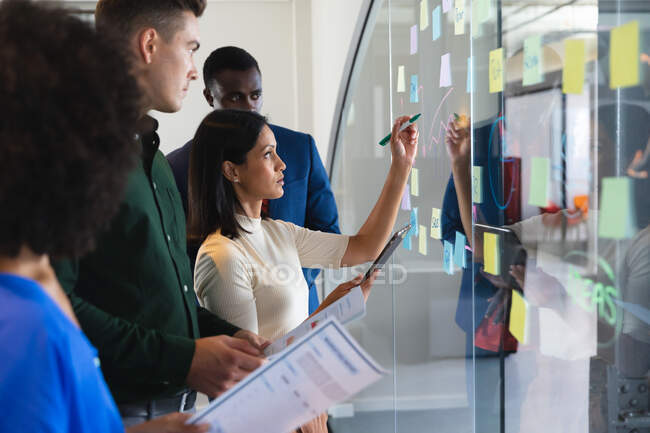 Team of diverse male and female office colleagues writing on glass board at modern office. business, professionalism, office and teamwork concept — Stock Photo