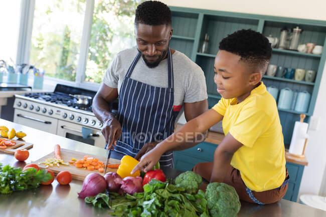 Père afro-américain et fils dans la cuisine, cuisiner ensemble. à domicile en isolement pendant le confinement en quarantaine. — Photo de stock
