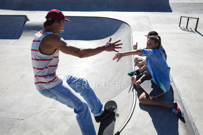 Três felizes amigos caucasianos do sexo feminino e masculino a andar de skate ao sol. sair em um parque de skate urbano no verão. — Fotografia de Stock