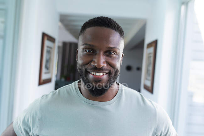 Retrato del hombre afroamericano mirando a la cámara y sonriendo. en casa en aislamiento durante el bloqueo de cuarentena. - foto de stock