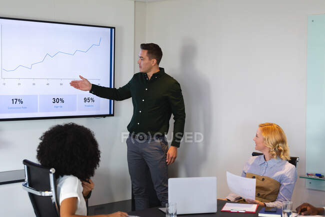 Hombre caucásico dando una presentación a sus colegas de oficina en la sala de reuniones en la oficina. negocio, profesionalidad, concepto de oficina y trabajo en equipo - foto de stock