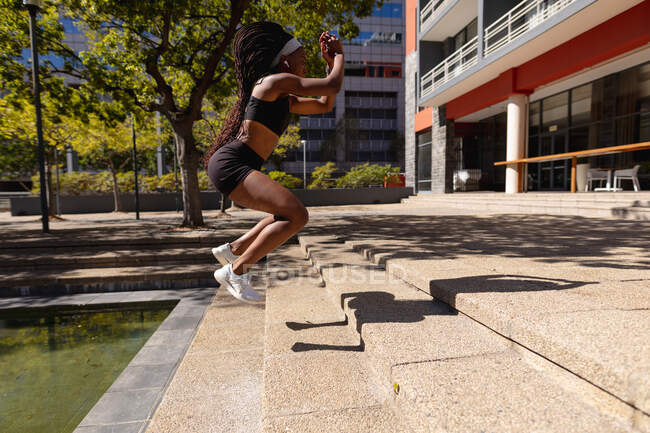 Fit femme afro-américaine sautant sur les marches de l'exercice en ville. mode de vie actif urbain sain et forme physique extérieure. — Photo de stock