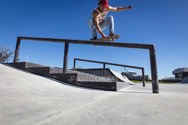 Hombre caucásico patinando en barandilla en un día soleado. pasando el rato en skatepark urbano en verano. - foto de stock