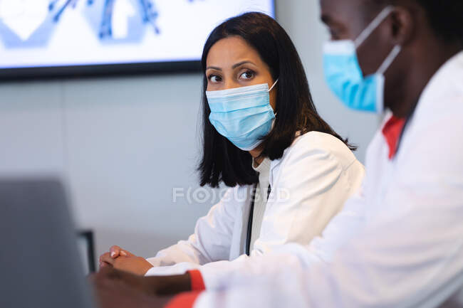 African american female doctor wearing face mask sitting in the meeting room. healthcare and medical research during covid 19 pandemic — Stock Photo