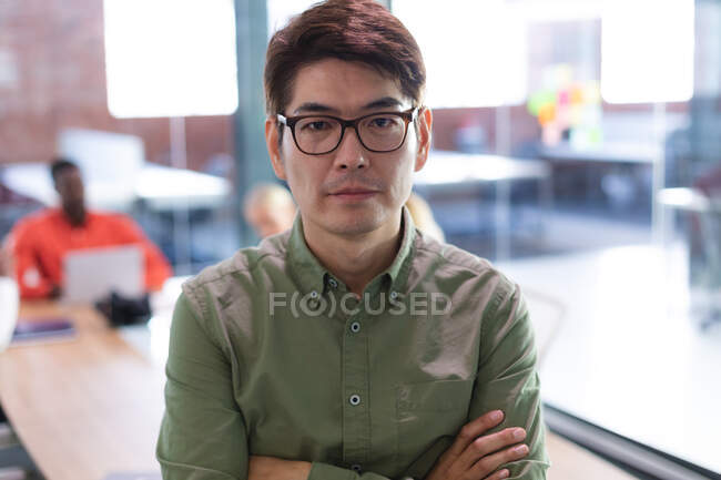 Retrato de hombre asiático con los brazos cruzados de pie en la oficina moderna. negocio, profesionalidad y concepto de oficina - foto de stock