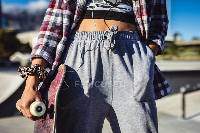 Mittelteil einer Frau, die mit dem Skateboard in der Sonne steht. Im Sommer im städtischen Skatepark abhängen. — Stockfoto