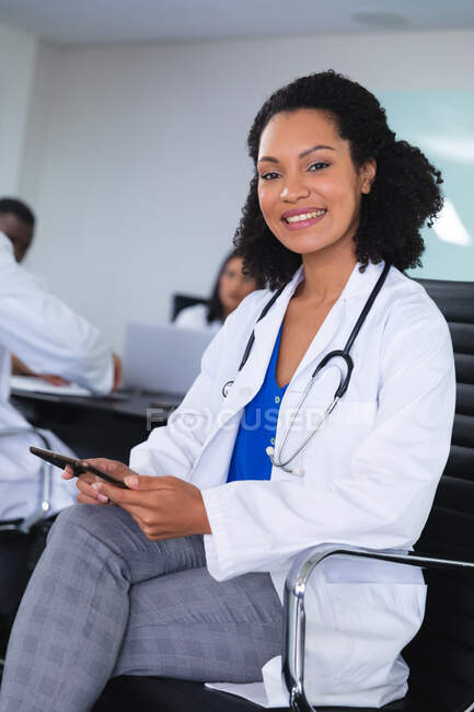 Porträt einer afrikanisch-amerikanischen Ärztin, die auf einem Stuhl im Besprechungsraum sitzt und lächelt. Gesundheits- und Professionalisierungskonzept — Stockfoto