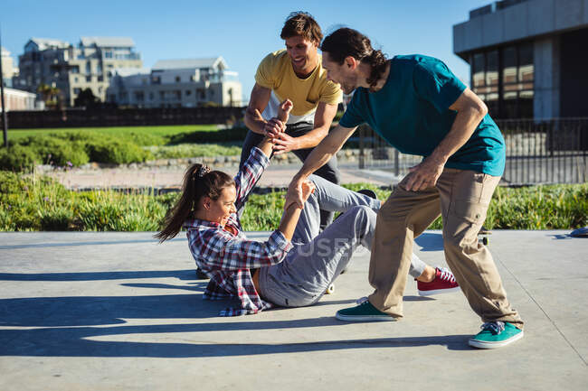Tres felices amigas caucásicas y hombres jugando al sol. pasando el rato en un skatepark urbano en verano. - foto de stock
