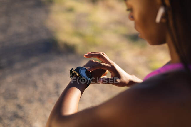 Adatto donna afro-americana che controlla smartwatch durante l'esercizio in campagna. sano stile di vita attivo e fitness all'aperto. — Foto stock