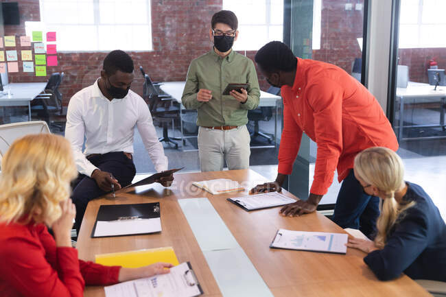 Une équipe de collègues de bureau masculins et féminins divers portant des masques faciaux discutant ensemble au bureau. hygiène et distanciation sociale sur le lieu de travail lors d'une pandémie de coqueluche 19. — Photo de stock