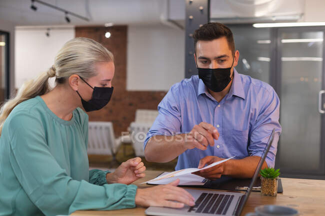 Des collègues de bureau blancs, hommes et femmes, portant des masques faciaux, discutent d'un document au bureau. hygiène et distanciation sociale sur le lieu de travail pendant la pandémie de covidé-19. — Photo de stock