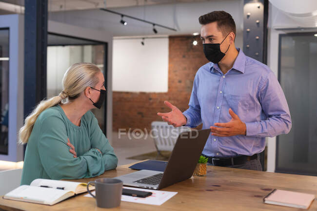 Colleghe caucasiche maschili e femminili che indossano maschere facciali che si parlano in ufficio. igiene e distanza sociale sul posto di lavoro durante la pandemia della covid-19. — Foto stock