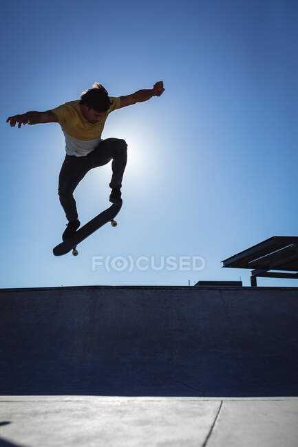 Uomo caucasico che salta e fa skateboard nelle giornate di sole. appendere fuori a skatepark urbano in estate. — Foto stock