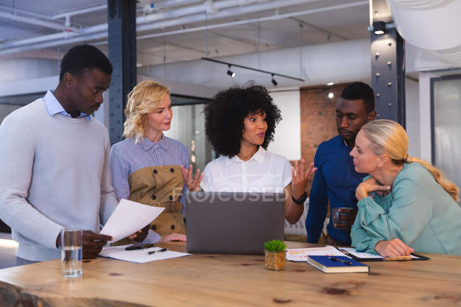 Team of diverse office colleagues discussing together over a laptop at modern office. business, professionalism, office and teamwork concept — Stock Photo