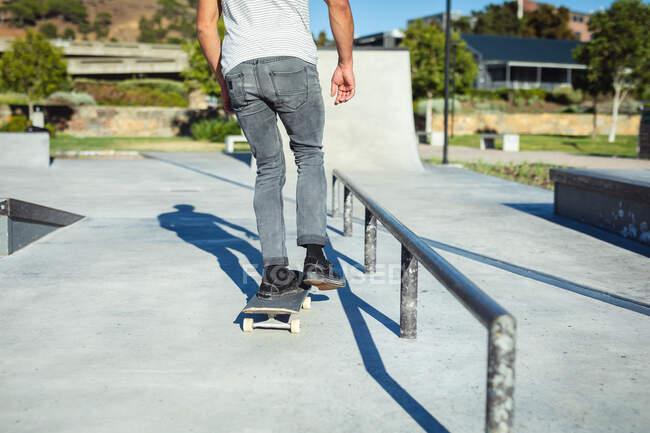 Baixa secção de homem a andar de skate ao sol. sair em um parque de skate urbano no verão. — Fotografia de Stock