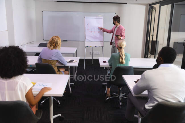 Asian man wearing face mask giving a presentation to his office colleagues in meeting room at office. hygiene and social distancing in the workplace during covid 19 pandemic. — Stock Photo