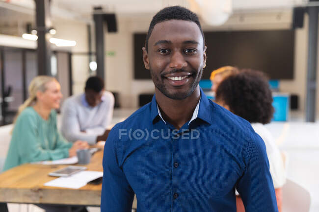 Retrato del hombre afroamericano sonriendo mientras estaba de pie en la oficina moderna. negocio, profesionalidad y concepto de oficina - foto de stock