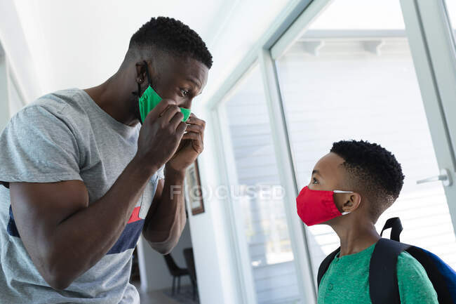 Père et fils afro-américains portant des masques. à domicile en isolement pendant le confinement en quarantaine. — Photo de stock