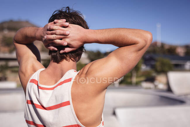 Rückenansicht eines kaukasischen Mannes, der die Hände hinter den Kopf legt. Abhängen im städtischen Skatepark im Sommer. — Stockfoto