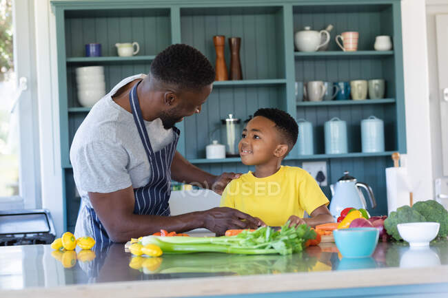Padre e hijo afroamericanos en la cocina, cocinando juntos. en casa en aislamiento durante el bloqueo de cuarentena. - foto de stock