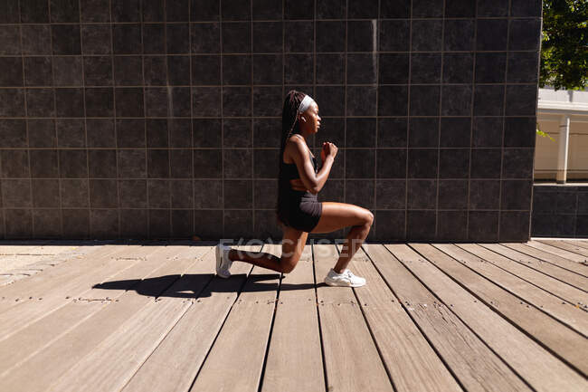 Ajuste mujer afroamericana haciendo saltos de ejercicio en la ciudad. estilo de vida activo urbano saludable y fitness al aire libre. - foto de stock
