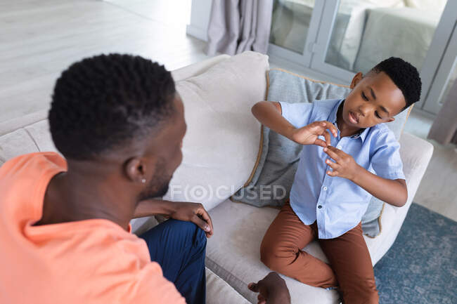 Afro-americanos pai e filho sentado no sofá, conversando em casa em isolamento durante o bloqueio de quarentena. — Fotografia de Stock