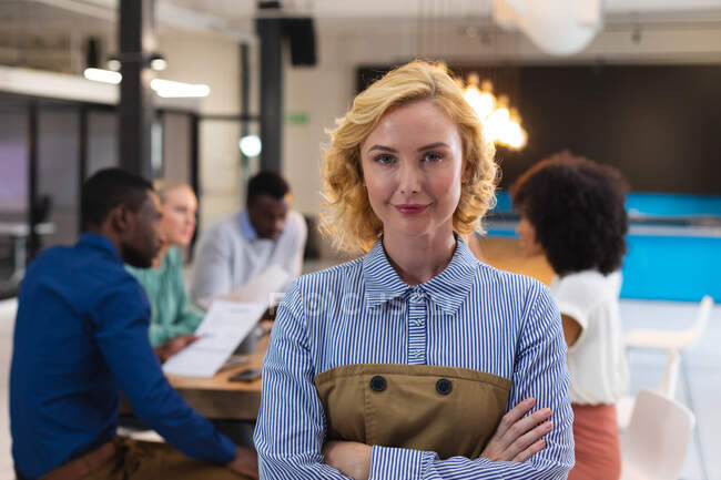 Retrato de mujer caucásica con los brazos cruzados de pie en la oficina moderna. negocio, profesionalidad y concepto de oficina - foto de stock