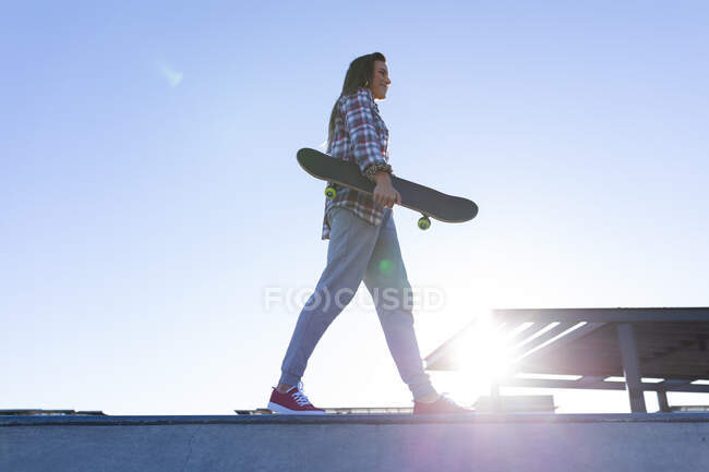 Porträt einer kaukasischen Frau, die mit dem Skateboard in der Sonne an der Wand läuft. Im Sommer im städtischen Skatepark abhängen. — Stockfoto