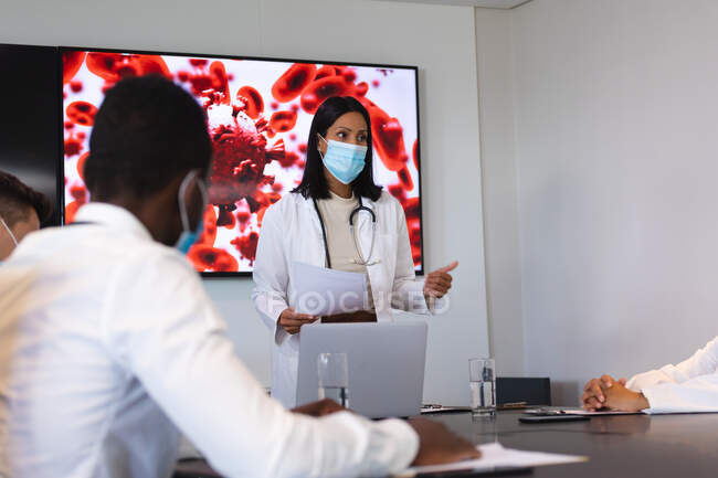 Medico donna che indossa maschera facciale dando presentazione al team di medici in sala riunioni. assistenza sanitaria e ricerca medica durante la pandemia della congrega 19 — Foto stock
