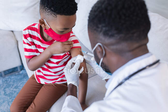 Medico afroamericano di sesso maschile con maschera facciale che vaccina il paziente ragazzo. medicinali, servizi sanitari e sanitari durante la pandemia di coronavirus covid 19. — Foto stock