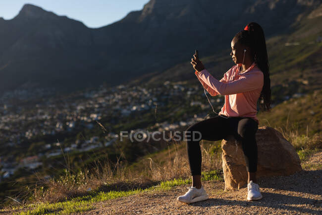 Mujer afroamericana tomando un descanso en el ejercicio al aire libre, tomando fotos con teléfono inteligente. estilo de vida activo saludable y fitness al aire libre. - foto de stock