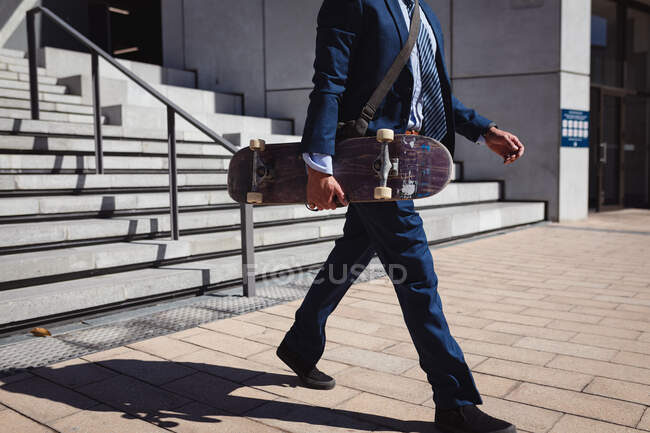 Niedriger Teil eines Geschäftsmannes mit Skateboard, der in der Sonne spazieren geht. Im Sommer im städtischen Skatepark abhängen. — Stockfoto