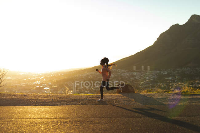 Fit african american woman running in countryside, wearing earphones. healthy active lifestyle and outdoor fitness. — Stock Photo