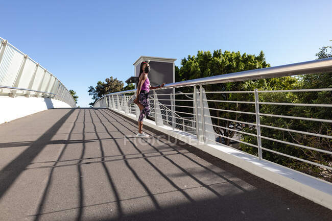 Жирна афро-американська жінка в масці, що тягнеться пішки по мосту, робить вправи в місті. Здоровий активний спосіб життя і пристосованість на відкритому повітрі під час коронавірусу covid 19 пандемії. — стокове фото