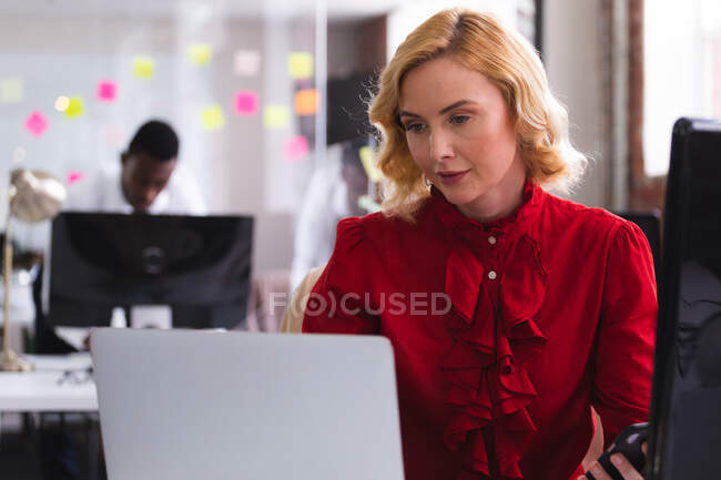 Кавказька жінка користується ноутбуком, сидячи на столі в сучасному офісі. бізнес, професіоналізм і офісна концепція — стокове фото