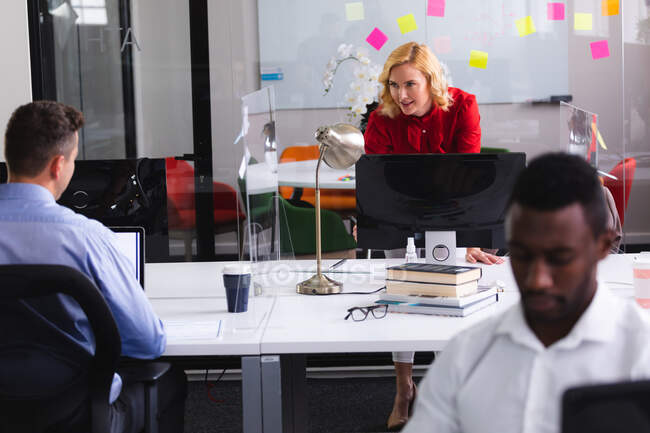 Mujer caucásica hablando con su colega masculino mientras está de pie cerca de su escritorio en la oficina. negocio, profesionalidad, concepto de oficina y trabajo en equipo - foto de stock