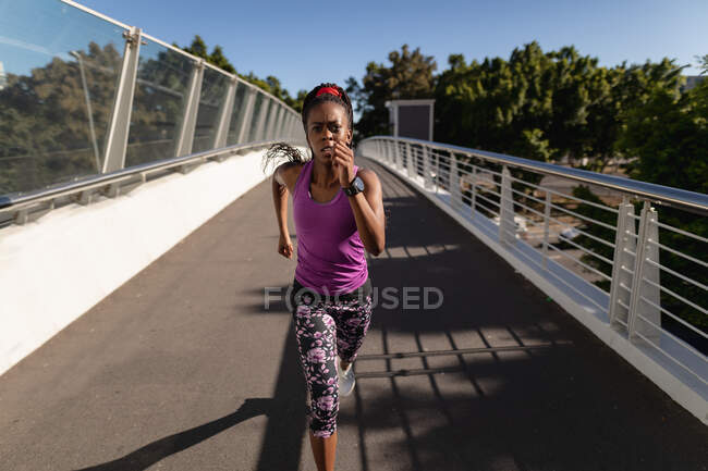 Подходящая африканская американка бегает по пешеходному мосту, тренируясь в городе. здоровый активный образ жизни и фитнес. — стоковое фото