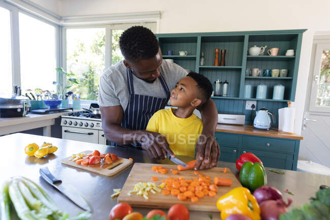 Padre e hijo afroamericanos en la cocina, cocinando juntos en casa en aislamiento durante el cierre de cuarentena. - foto de stock