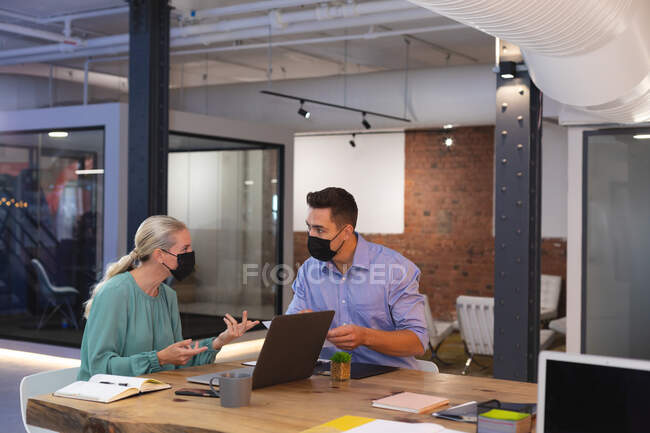 Caucasian male and female office colleagues wearing face masks talking to each other at office. hygiene and social distancing in the workplace during covid-19 pandemic. — Stock Photo