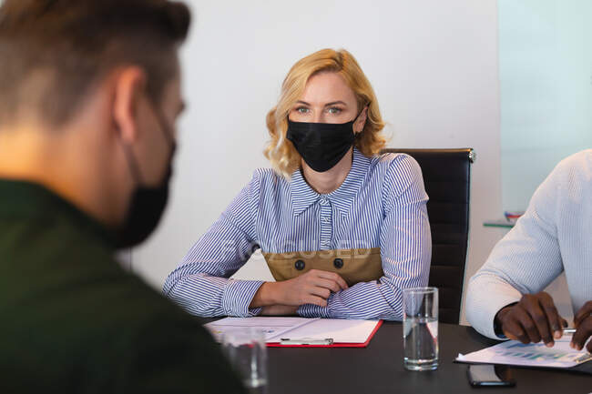 Caucasian woman wearing face mask sitting in meeting room at modern office. hygiene and social distancing in the workplace during covid 19 pandemic. — Stock Photo