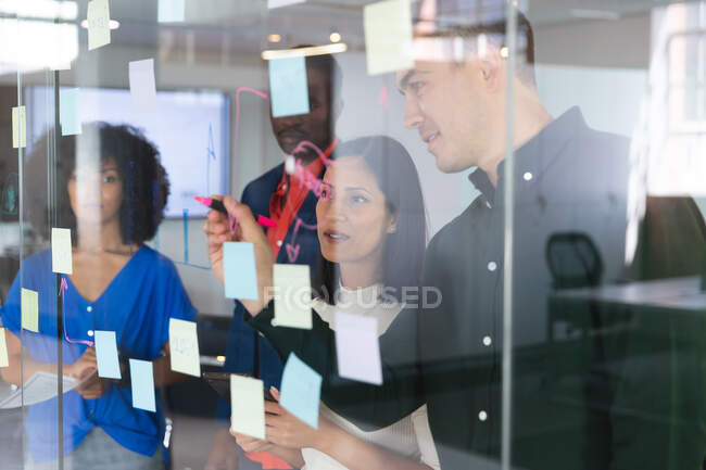Team of diverse male and female office colleagues writing on glass board at modern office. business, professionalism, office and teamwork concept — Stock Photo