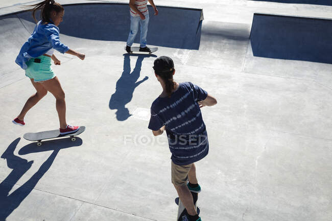 Drei glückliche kaukasische Freundinnen und Freunde skateboarden in der Sonne. Im Sommer im städtischen Skatepark abhängen. — Stockfoto