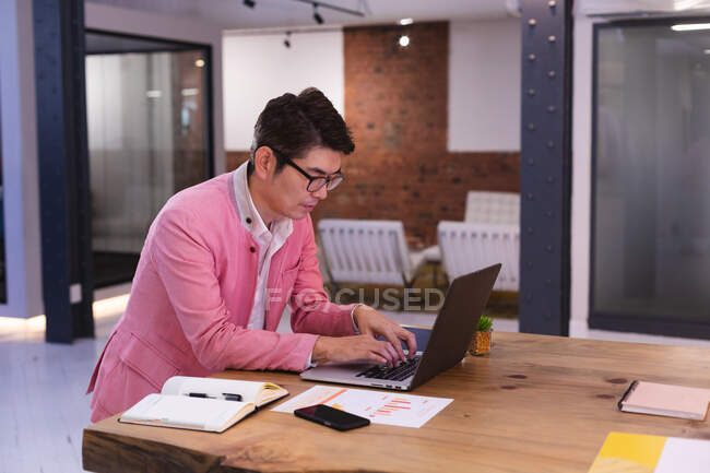 Азіатський чоловік друкує на ноутбуці, працюючи в сучасному офісі. бізнес, професіоналізм і офісна концепція — стокове фото